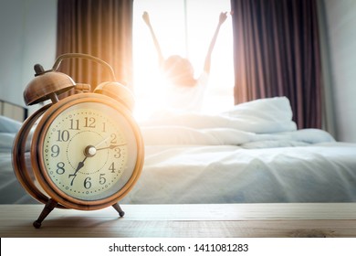 Morning Of A New Day, Alarm Clock Wake Up Woman Sitting In The Room. A Woman Stretch The Muscles At Window. Health And Care Concepts