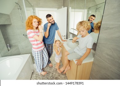 In The Morning. Nice Pleasant Family Standing Together In The Bathroom While Brushing Their Teeth In The Morning