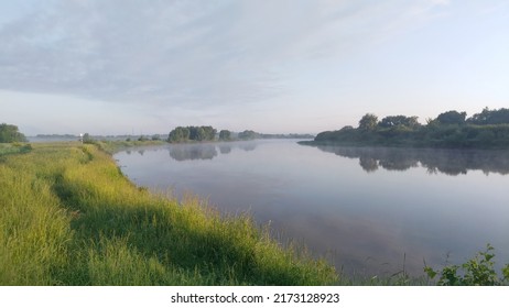 Morning on the river. Light fog and soft sunshine. Tall grass and trees grow along the banks and are reflected in the calm water. There is a slight cloudiness in the sky - Powered by Shutterstock