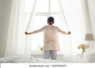 Morning And People Concept - Happy African American Woman Opening Window Curtains At Home Bedroom
