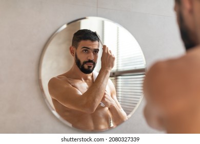 Morning Preparation. Portrait Of Handsome Young Guy Brushing His Glossy Hair, Looking At Reflection In Mirror, Rear Back Over The Shoulder View. Confident Arab Man Making Hairstyle Using Wooden Brush