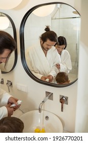 In The Morning. Reflection At The Mirror Of The Nice Pleasant Family Standing Together In The Bathroom While Brushing Their Teeth In The Morning. Stock Photo