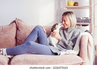 Morning Relaxation. Smiling middle-aged 40s woman Sitting in couch And Enjoying against Window. Female play with dog, pet licks girl - Powered by Shutterstock