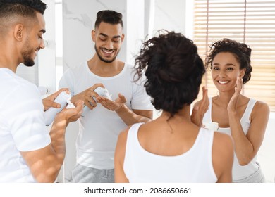 Morning Rituals. Happy Arab Couple Making Self-Care Routine Near Mirror In Bathroom, Middle Eastern Lovers Getting Ready Together, Man Using Shaving Foam While Woman Applying Moisturising Cream