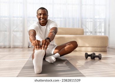 Morning routine. Athletic millennial black man warming up and stretching, preparing for workout with dumbbells, training on mat in living room interior at home, free space. - Powered by Shutterstock