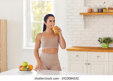 Morning Routine. Beautiful Fitness Woman In Sportswear Drinks Fresh Fruit Juice After Workout Standing At Home In The Kitchen. Concept Of A Healthy Diet And Vitamins.