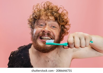 Morning Routine. Portrait Of Cheerful Man In Character Of Neanderthal Brushing Teeth With Toothpaste Isolated Over Pink Background. Concept Of History, Modern And Ancient Combination, Evolution And Ad