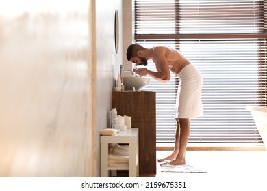 Morning Routine. Profile Side View Portrait Of Attractive Muscular Bearded Man With Naked Torso Washing Up His Face With Water Standing Near Sink Tap. Nude Guy Getting Ready, Full Body Length