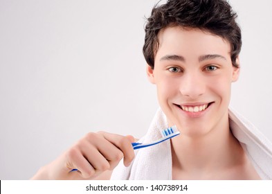 Morning routine of washing the teeth. Handsome young man with beautiful teeth smiling and holding a toothbrush.