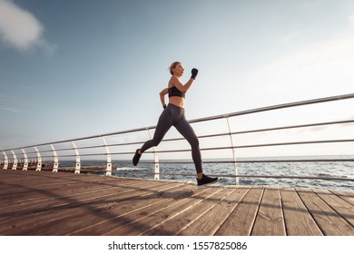 Morning run. Young athletic woman in sportswear runs on the beach at sunrise. Outdoor workout. Healthy lifestyle - Shutterstock ID 1557825086
