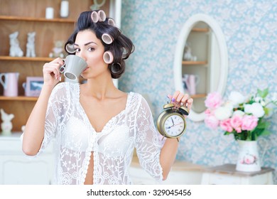 Morning Rush. Beautiful Woman In Hair Curlers Drinking Coffee And Holding A Clock In Her Hand