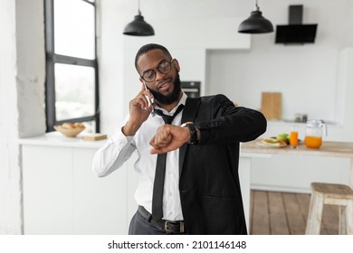 Morning Rush. Busy African American business man worker in eyeglasses talking on smart phone at home, wearing suit and looking at wrist watch, getting ready, going to office in a hurry, being late