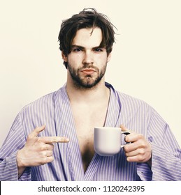 Morning And Showering Concept. Guy Or Sportsman In Home Or Bath Clothes Drinks Tea Or Coffee. Man With Beard In Blue Dressing Gown On Grey Background. Macho In Bathrobe Points At Mug In Hand.