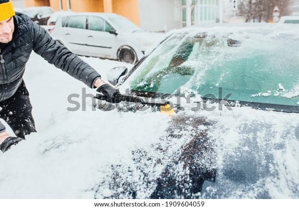 Morning snow removal - a man cleans the car before\
the trip - cold start in\
winter