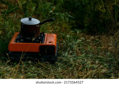 In the morning spring twilight, there is a gas cylinder with a burner on the river bank. On it, water is boiled in a teapot for brewing tea. Camping. Nature. - Shutterstock ID 2173364527