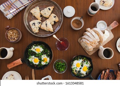 Morning Still Life Of Fresh, Farm To Table Breakfast Or Brunch Spread Flat Lay, With Scones On Plate, Cast Iron Skillet With Baked Eggs, Coffee, Bread On Cutting Boards, Bacon On Top Of Wooden Table