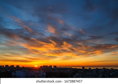 The morning sun rises over the horizon and turns the clouds golden orange. Dawn fire in the sky over a small seaside city. Scenic landscape at sunrise. Beauty in nature.
