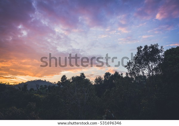 Morning sun rising at nice view of\
misty mountains. Road to mountains with clouds in blue\
sky.