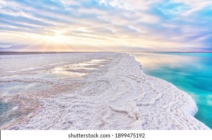 Morning sun shines on salt crystals formations, clear cyan green calm water near, typical landscape at Ein Bokek beach, Israel