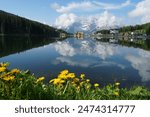 Morning view of Lake Misurina, reflection on the water, sky and summer flowers of the Dolomites. Northern Italy