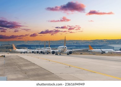 Morning view of a queue of planes ready for takeoff taxiing on the runway, against the backdrop of a beautiful sky at dawn sunrise