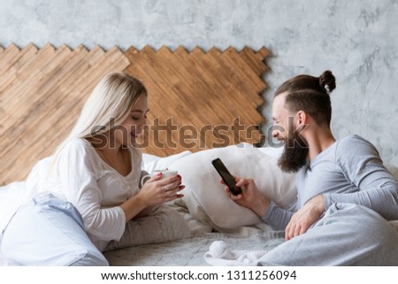 Morning wake up ritual. Smiling man and woman in bed with drink and smartphone.