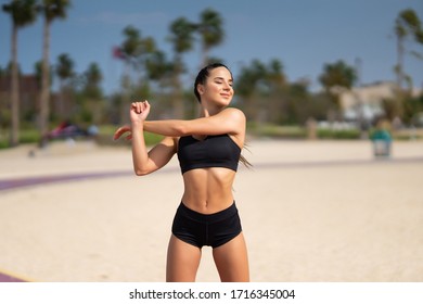 Morning workout. Young fit woman in sportswear doing hand stretching on the beach at sunrise - Powered by Shutterstock