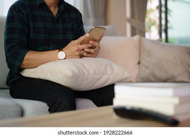 In The Morning Young Business Man Sat On The Sofa In The Living Room At Home, Using The Phone To Check And Reply To Email.