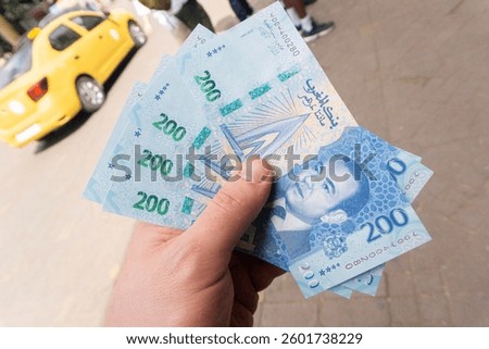 Moroccan currency background. Dirham banknotes fanned out in hand. Cash on the street with a taxi in the background. Foreign money symbolizing travel expenses and vacation costs in Africa.