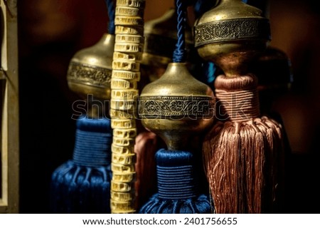 Moroccan curtain ties made with blue and orange tassles attached to a brass ornament with intricate design.