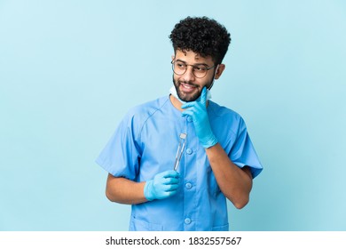 Moroccan dentist man holding tools isolated on blue background thinking an idea while looking up
