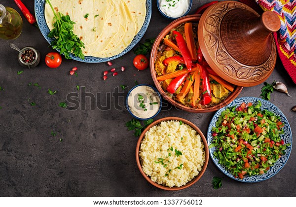 Moroccan food. Traditional
tajine dishes, couscous  and fresh salad  on rustic wooden table.
Tagine chicken meat and vegetables. Arabian cuisine. Top view. Flat
lay