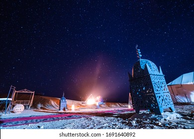 Moroccan lantern of a base camp in the middle of the desert with bonfire in the background and starry night sky - Powered by Shutterstock