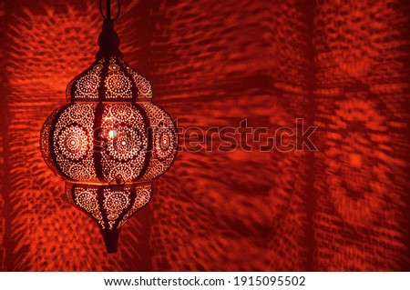 Moroccan lantern with red illuminating patterns of light on textured wall in horizontal position. 