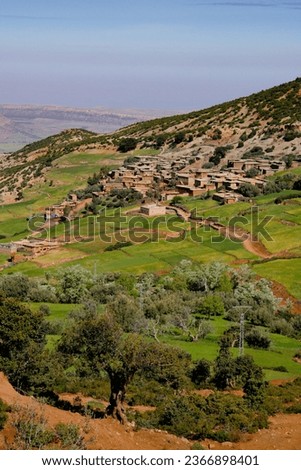 In Morocco, a mountain village in the High Atlas. In the foreground are olive trees, then cultivated fields. The houses are built of red earth. In the background, the mountains.