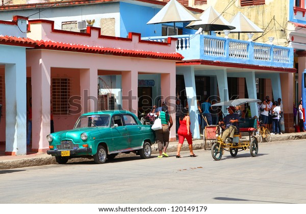 MORON, CUBA - FEBRUARY 19: People walk past old car\
on February 19, 2011 in Moron, Cuba. Recent change in law allows\
the Cubans to trade cars again. Cars in Cuba are very old because\
of the old law.