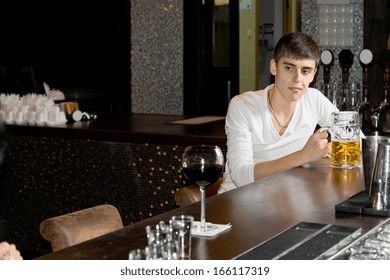 Morose drunk young man drinking beer sitting alone at the bar with a large tankard of draught in front of him