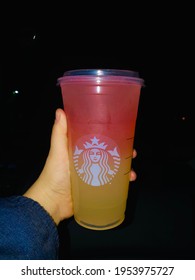 Morristown, New Jersey USA- April 7th, 2021: Image Of A Person Holding Pink And Yellow Venti Raspberry Lemonade Starbucks Drink In Her Hand In Front Of A Black Background 