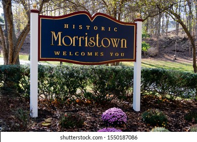 Morristown, NJ / USA - 11/2/19: Historic Morristown Welcomes You Blue Red And Gold Leaf Sign With White Posts, Various Flowers, Shrubbery And Trees In The Forefront And Background