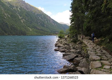 Morskie Oko Lake - The Largest Lake In The Tatra Mountains. A Mountain Chalet By The Lake. People On The Hiking Trail Along The Morskie Oko Lake