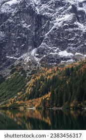 Morskie Oko, Poland: Majestic cliffs dusted with snow tower above a serene lake. Autumn's vibrant hues paint the forest, mirrored flawlessly in the tranquil waters. Nature's pristine beauty unveiled. - Shutterstock ID 2383456317