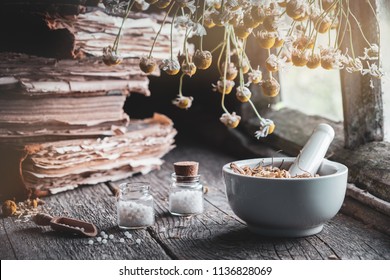 Mortar of dried healing herbs, bottles of homeopathic globules, old books and bunch of dry chamomile plant. Homeopathy medicine. 