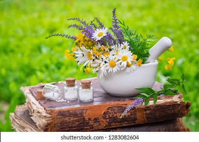 Mortar of healing herbs, bottles of homeopathic globules and old book outdoors. Homeopathy medicine.