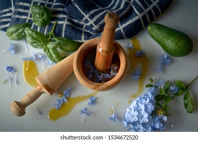 Mortar And Pestle Making Essential Oils With Blue Flower Petals And Avocado With Basil On White Marble