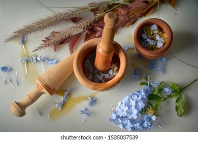 Mortar And Pestle Making Essential Oils With Blue Flower Petals And Avocado With Basil On White Marble