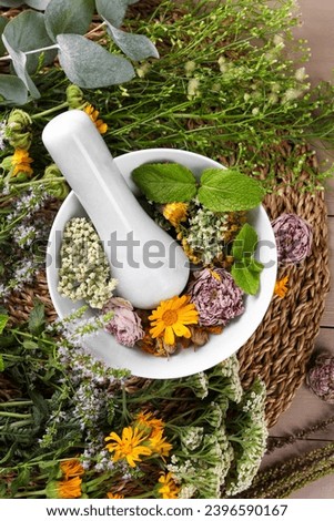 Mortar with pestle and many different herbs on table, flat lay