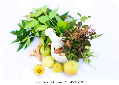 Mortar And Pestle With Tulsi Leaves(Basil) Neem Leaves,Indian Amla(Gooseberry), Dry Ginger Etc. On White Background. Trivandrum, Kerala, India.