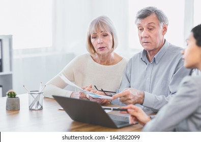 Mortgage Calculator. Focused Senior Couple Comparing Current Refinance Interest Rates With Financial Adviser At Office