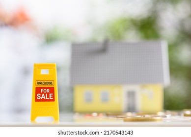 Mortgage Foreclosure Sales, Financial Concept : Yellow Warning Or Sign Board With The Words FORECLOSURE FOR SALE, A Model House And Coins On A Table, Depicting Lender Takes Possession Of The Mortgage.