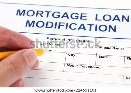 Mortgage Loan Modification application form and human hand with pencil.